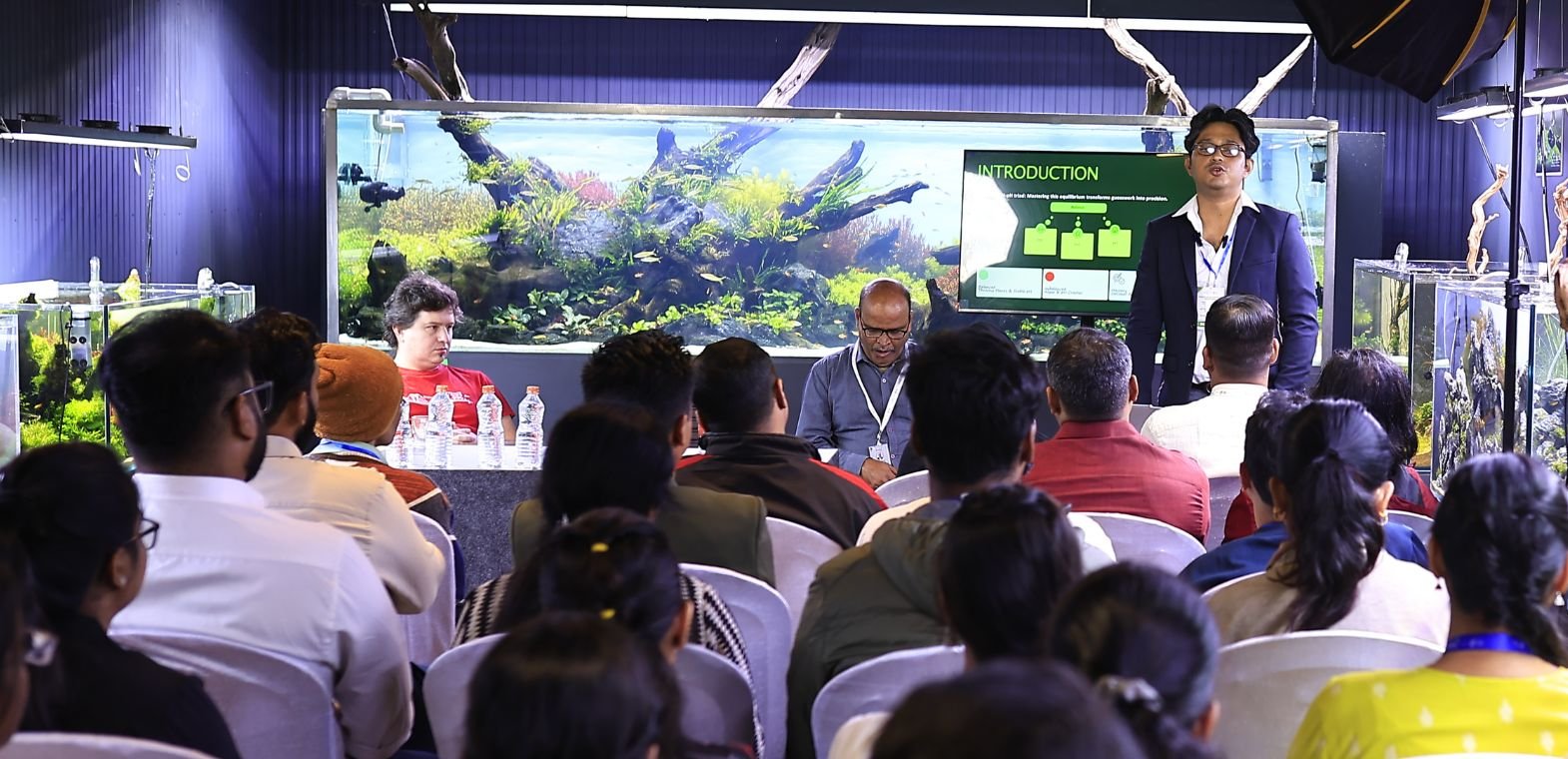Speaker presenting at a professional Terrarium and Amphibian Workshop at TiCi NatureLab, with attendees participating in an educational session surrounded by large nature aquariums and aquascaped ecosystem displays.