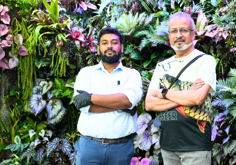Two nature enthusiasts standing in front of a lush vertical rainforest wall at TiCi NatureLab, surrounded by tropical plants, ferns, begonias, orchids and biophilic green wall installations.