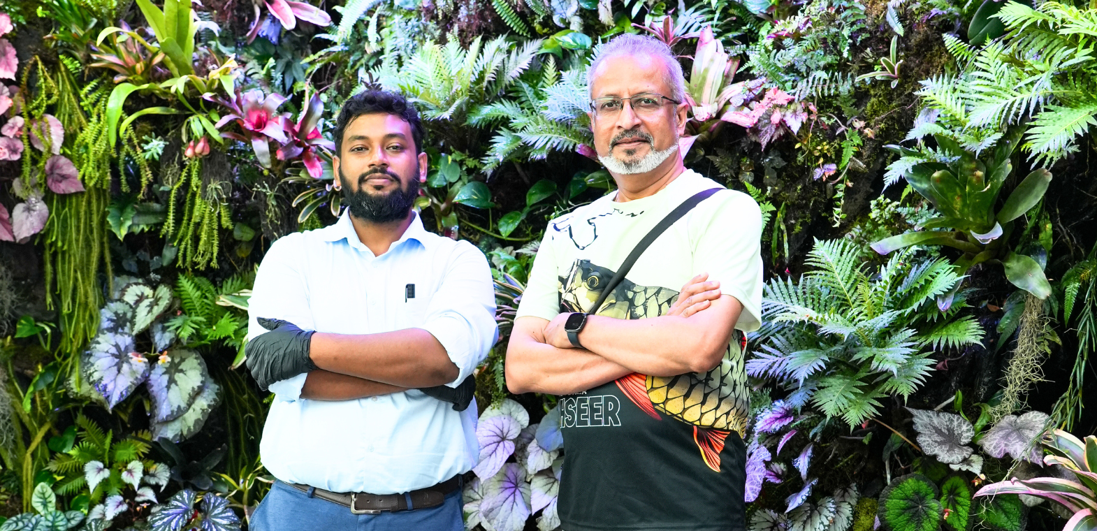 Two nature enthusiasts standing in front of a lush vertical rainforest wall at TiCi NatureLab, surrounded by tropical plants, ferns, begonias, orchids and biophilic green wall installations.
