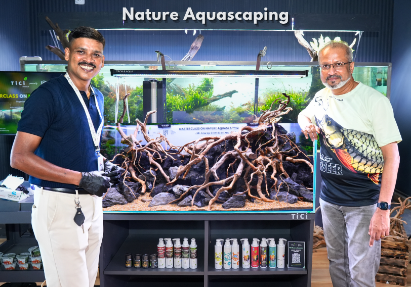 Aquascaping experts pose beside a completed hardscape aquarium during the Nature Aquascaping MasterClass at TiCi NatureLab, showcasing an intricate layout of spider wood and lava rocks designed for a nature-inspired freshwater aquascape.